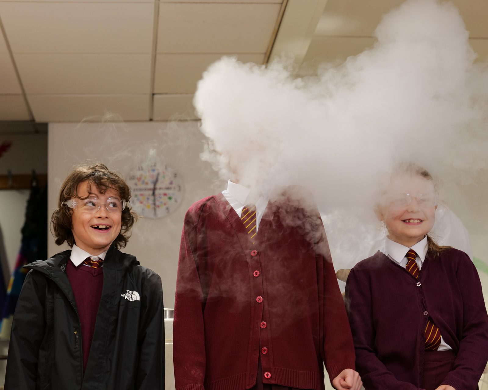 Three children in school uniform with their heads enveloped in clouds laughing