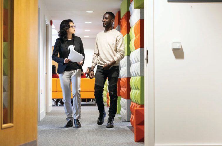 A student and lecturer talking to each other whilst walking down a corridor