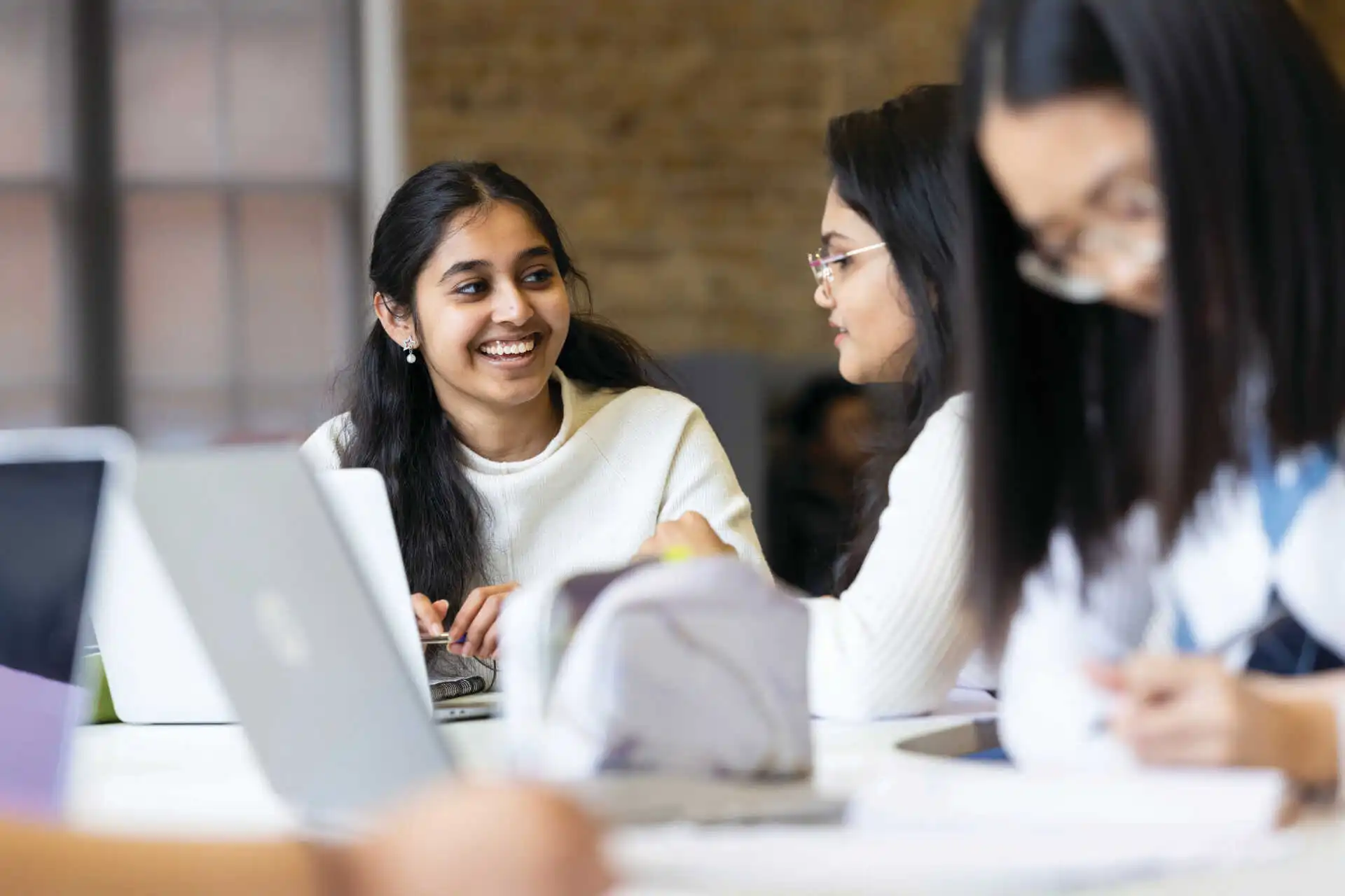 Three female students chatting and laughing whilst working on their laptops